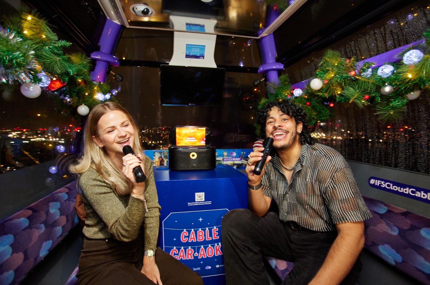 Two guests singing inside a Cable Car-aoke cabin above the London skyline at night